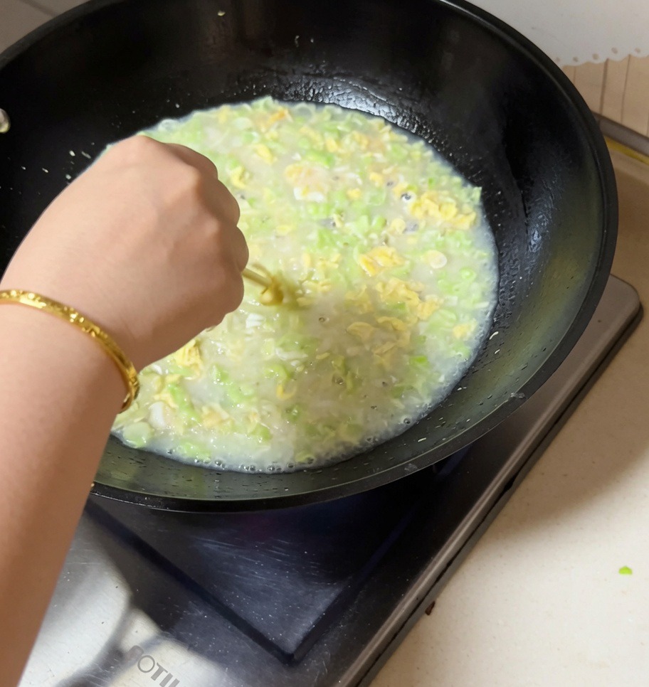 Eine Hand rührt mit Stäbchen in einem kochenden Wok mit Muschel-Bohnen-Eier-Suppe.