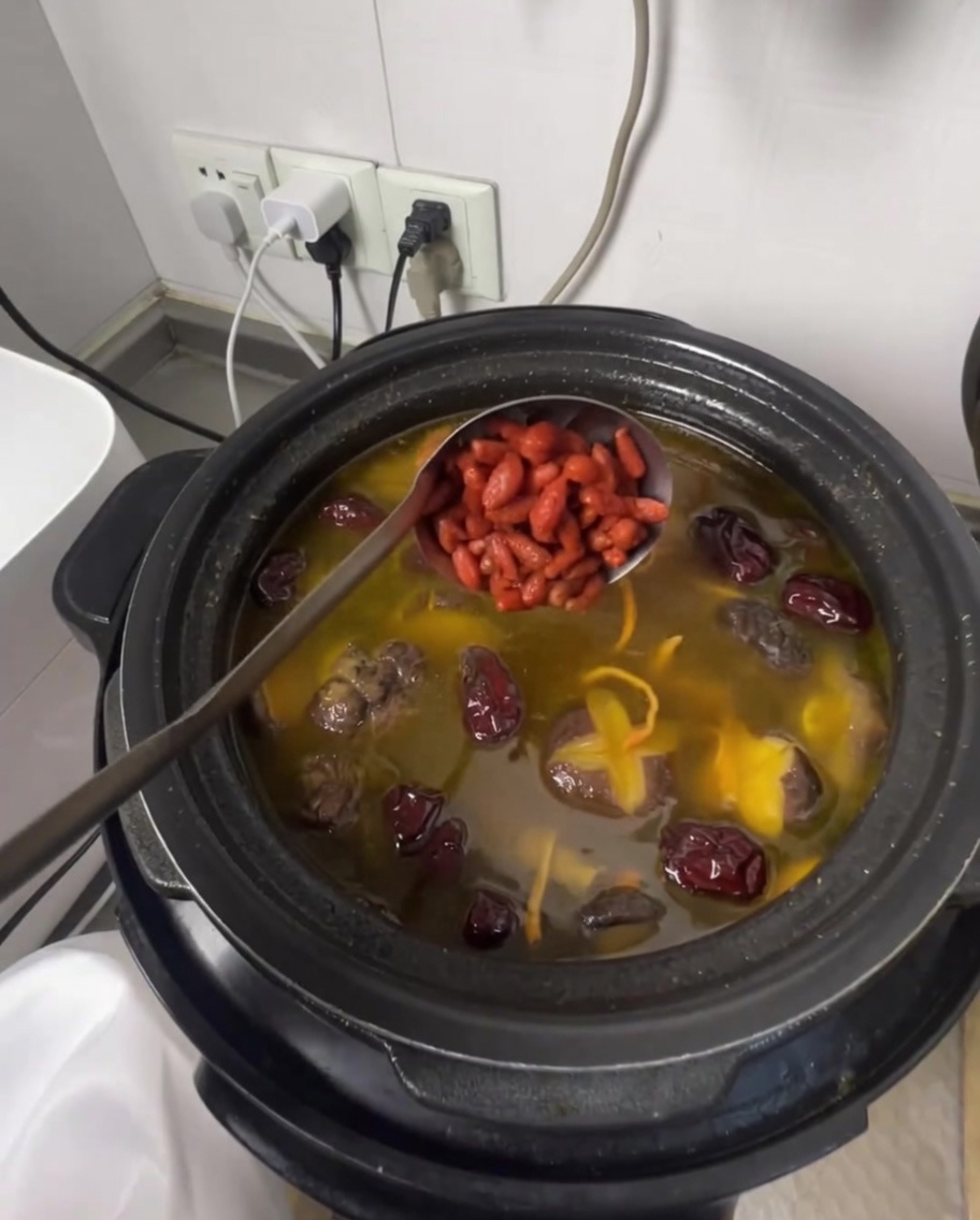 Eine Schöpfkelle gibt Goji-Beeren in die duftende Hühnersuppe.
