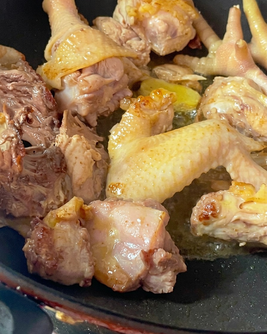 Rohe Stücke vom Suppenhuhn werden in einem heißen Wok ohne Öl angebraten, um Feuchtigkeit zu entziehen.