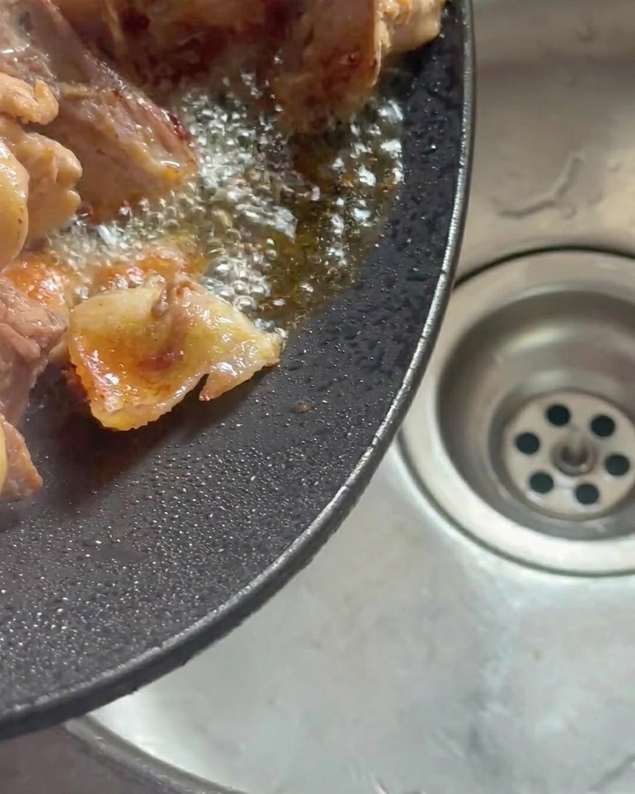 Ein geneigter Wok, aus dem ausgelassenes Hühnerfett in eine Spüle gegossen wird.