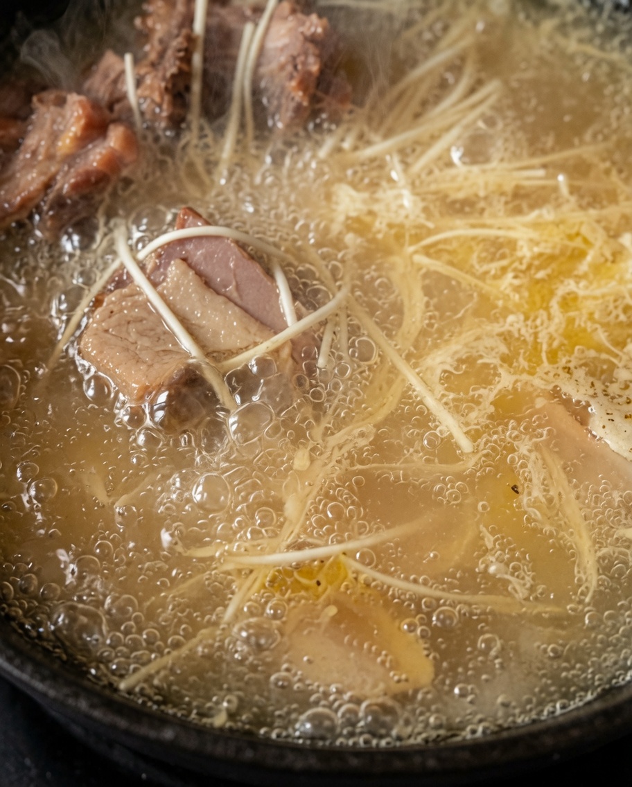 Nudeln kochen in einem Topf mit blubbernder, reichhaltiger weißer Hühnersuppe.