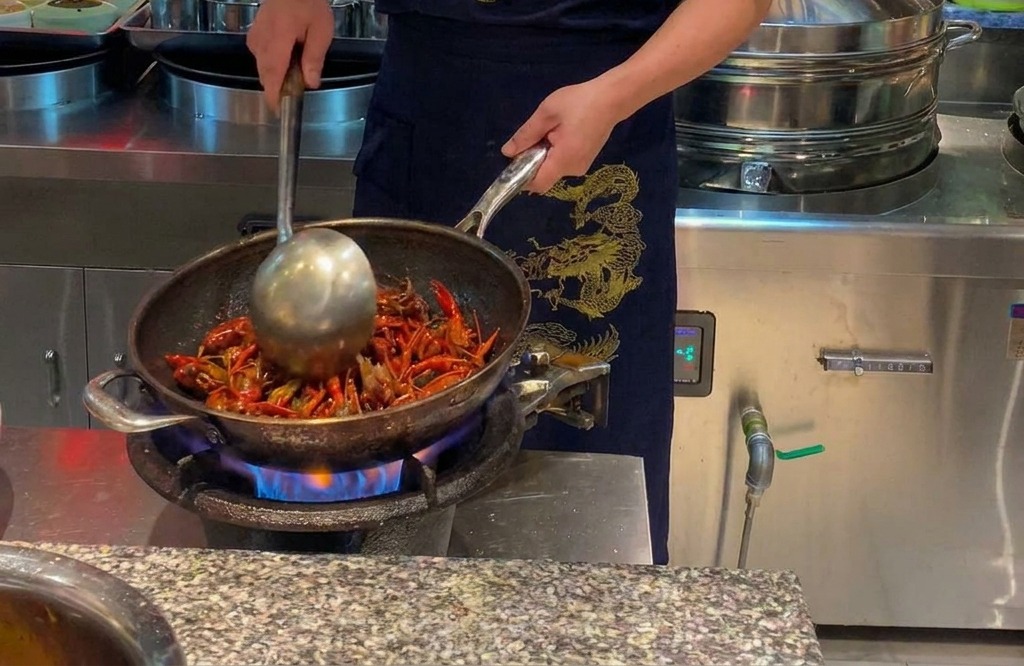 Ein Koch brät leuchtend rote Flusskrebse in einem großen Wok über offener Flamme.