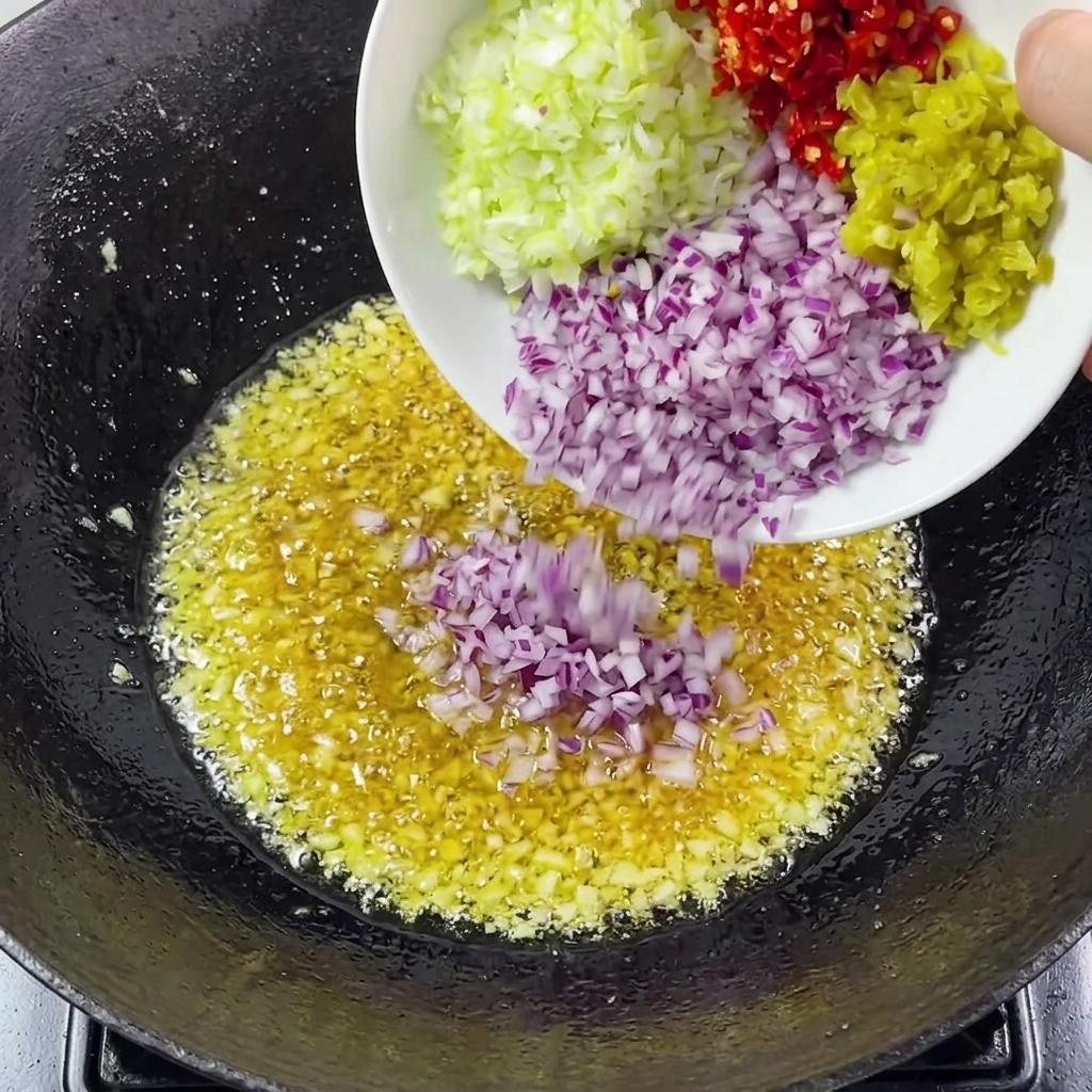 Gehackte Zwiebeln, Frühlingszwiebeln und Chilis werden zum Knoblauch in den Wok gegeben.