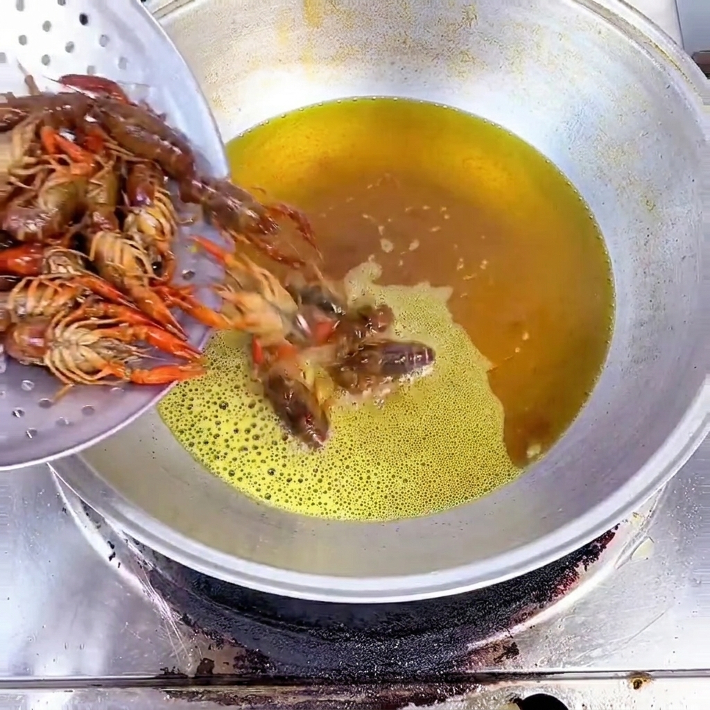 Geputzte Flusskrebse werden aus einem Metallsieb in einen Wok mit heißem, gelbem Öl gegeben.
