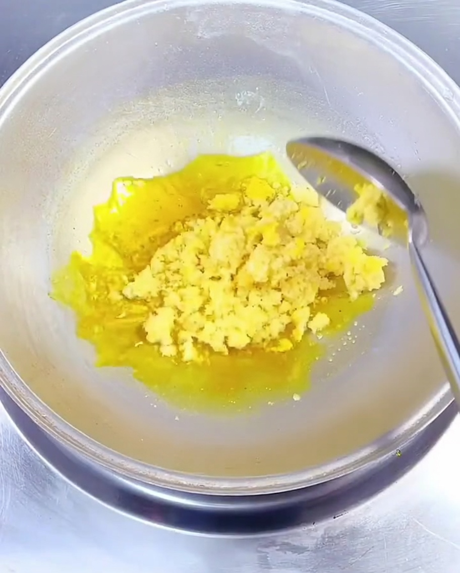 Gehackter Knoblauch wird mit einem Metalllöffel in heißem, gelbem Rapsöl im Wok umgerührt.
