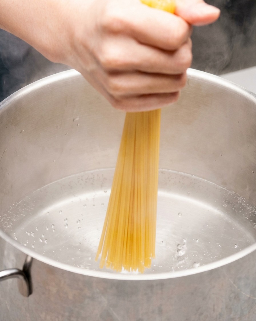 Eine Hand drückt Spaghetti in einen Topf mit kochendem Wasser.
