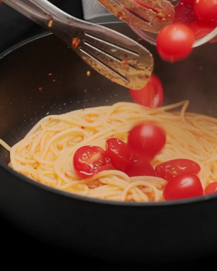 Halbierte Kirschtomaten werden zu den Spaghetti in die Pfanne gegeben.