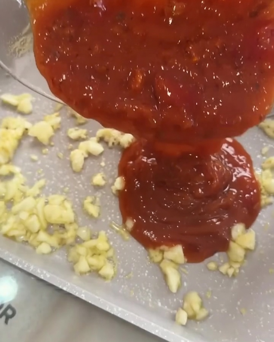 Würzige Tomaten-Fleischsauce wird zum angebratenen Knoblauch in die Pfanne gegossen.