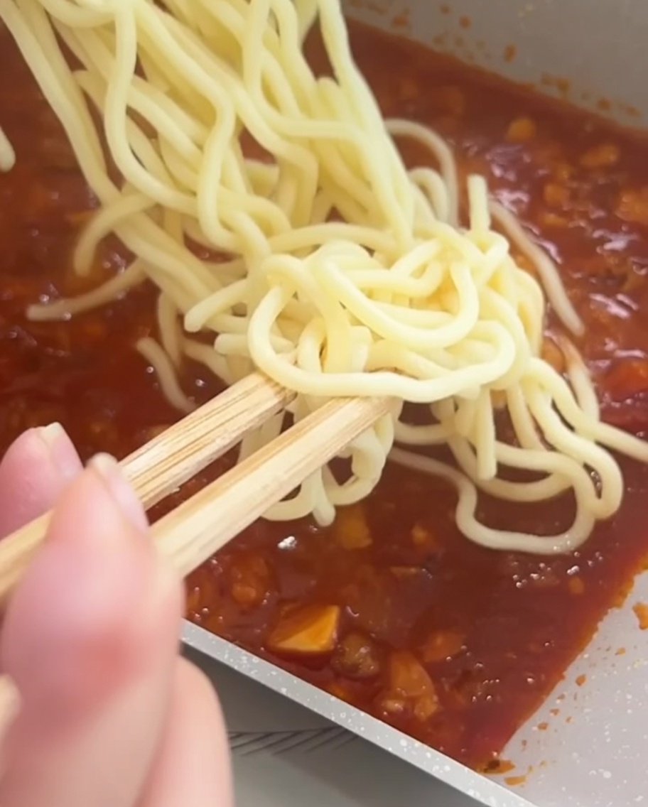 Spaghetti werden mit Essstäbchen in der Pfanne gründlich mit der Fleischsauce vermischt.