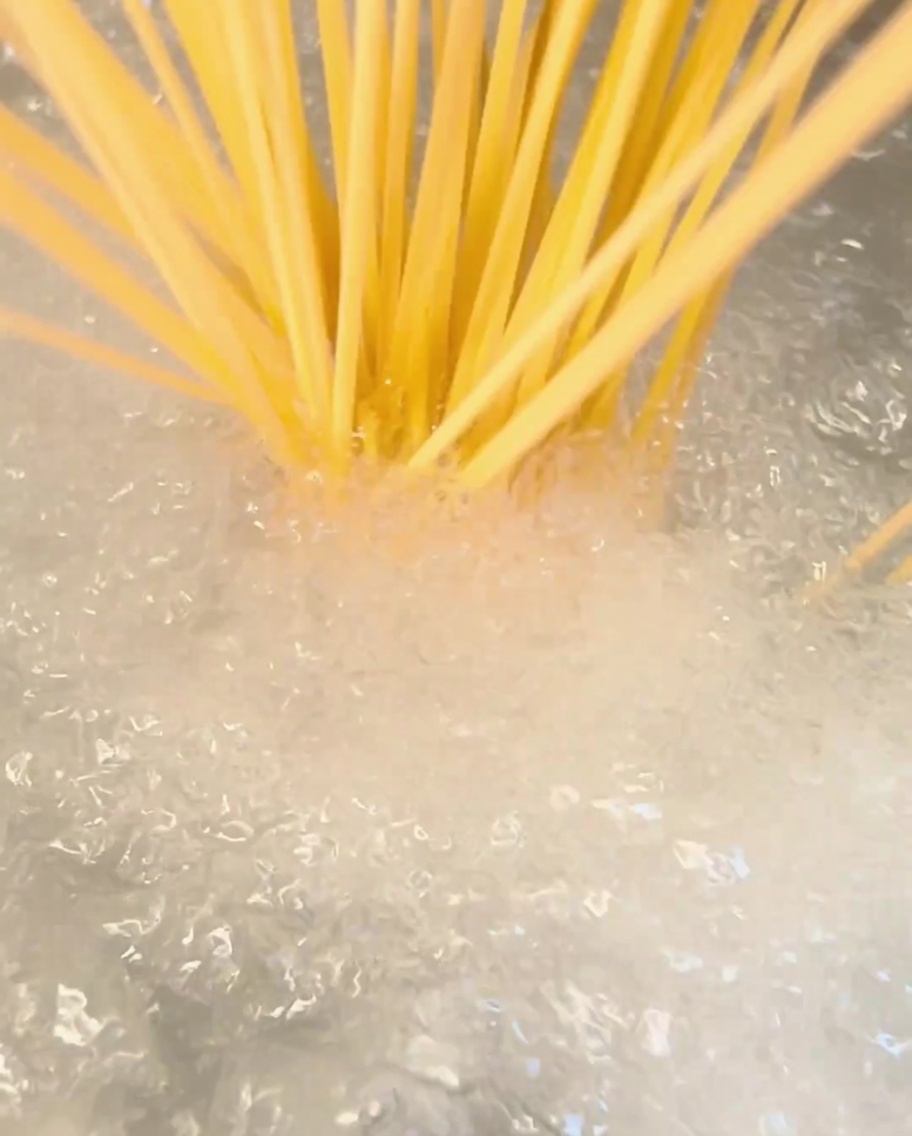 Ein Bündel trockener Spaghetti wird in einen Topf mit kochendem Wasser gegeben.