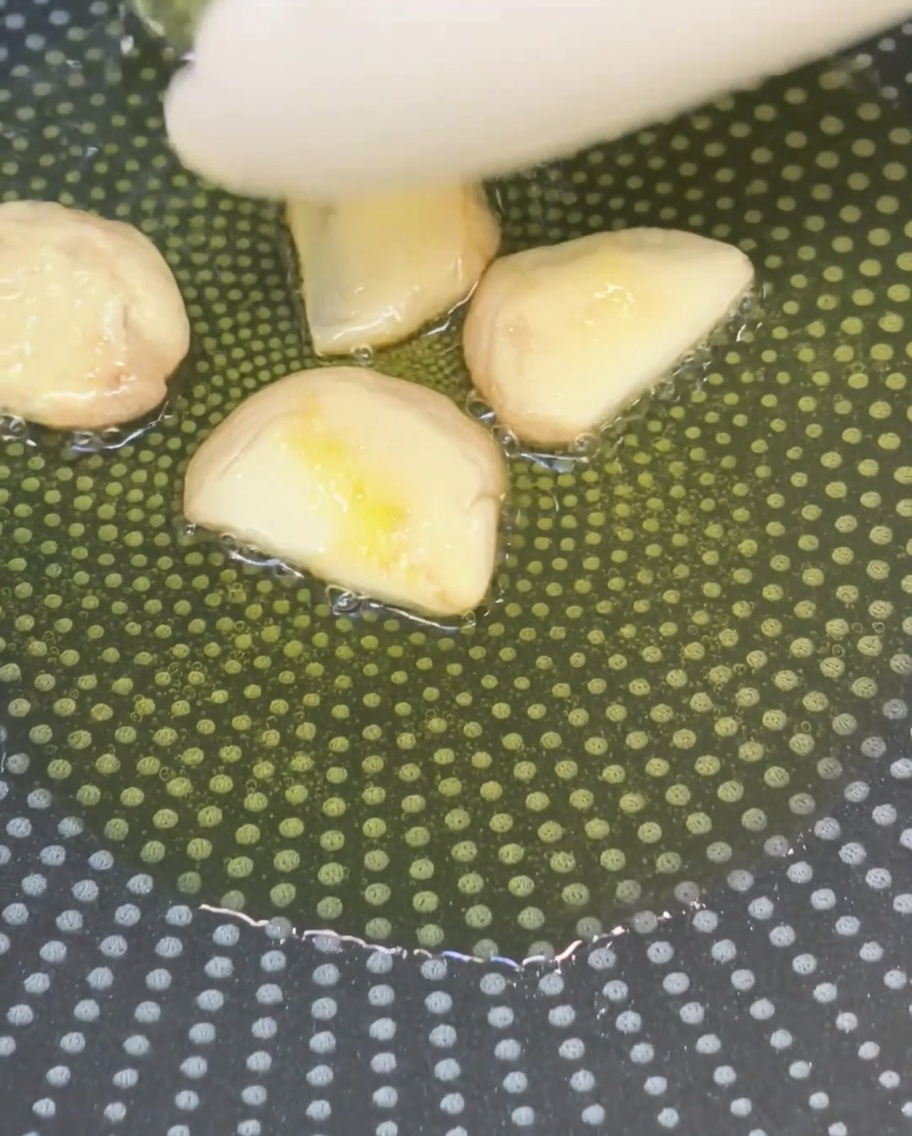 Zerdrückte Knoblauchzehen braten in Olivenöl in einer beschichteten Pfanne.