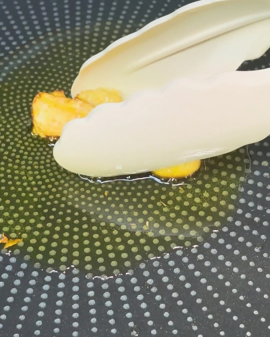 Eine Zange holt goldbraun gebratenen Knoblauch aus dem Öl in einer Pfanne.