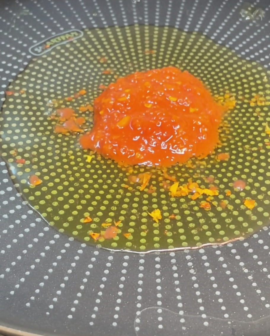 Ein Haufen leuchtend roter, stückiger Tomaten in der Mitte einer Pfanne mit gewürztem Olivenöl.