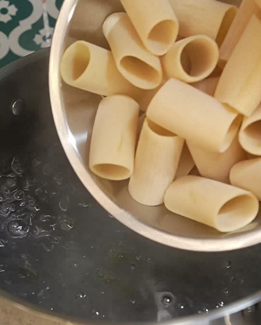 Trockene Rigatoni werden in einen Topf mit sprudelnd kochendem Wasser geschüttet.