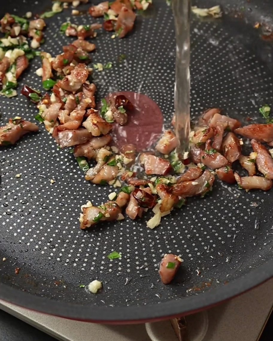 Heller Weißwein wird über den heißen Speck und die Kräuter in die Pfanne gegossen.
