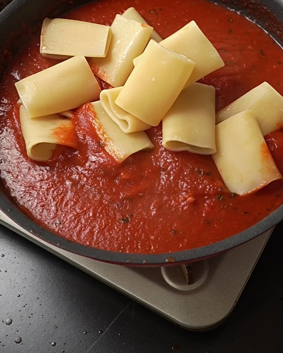 Gekochte Rigatoni werden in die Pfanne mit der leuchtend roten Soße gegeben.