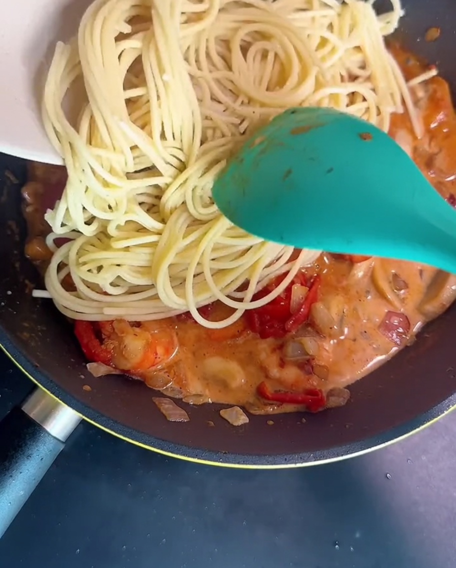 Spaghetti werden in der Pfanne mit der Garnelen-Pilz-Sauce geschwenkt.