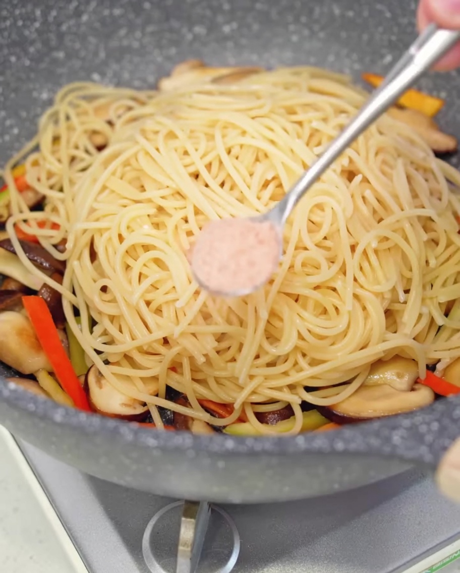 Etwas Salz wird über die Spaghetti in der Pfanne gestreut.
