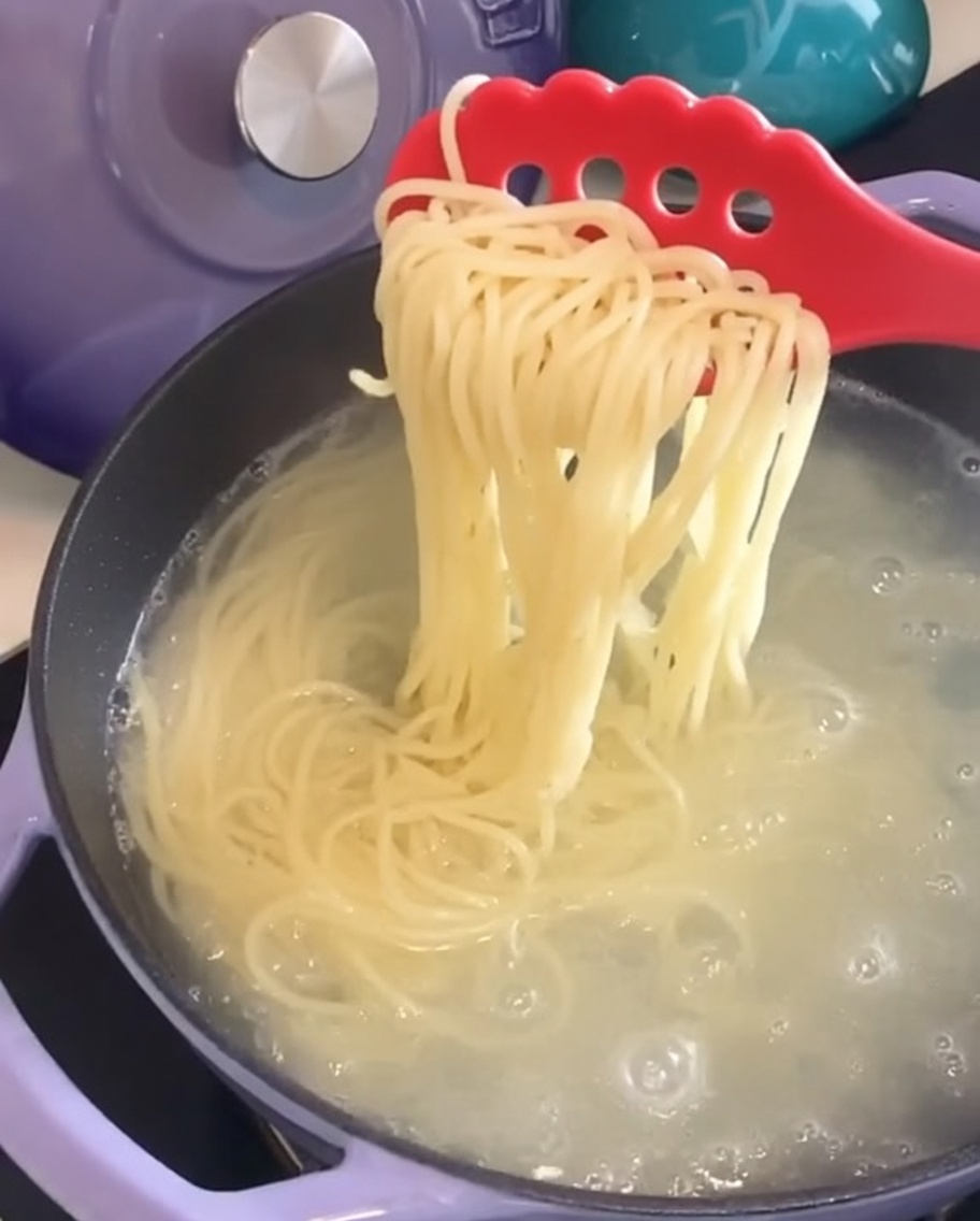 Gekochte Spaghetti werden mit einer Nudelzange aus dem Wasser gehoben.