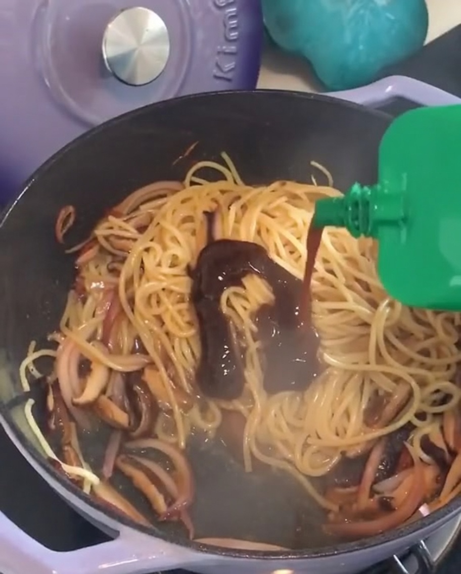 Schwarze Pfeffersauce wird über die Nudeln gegeben.
