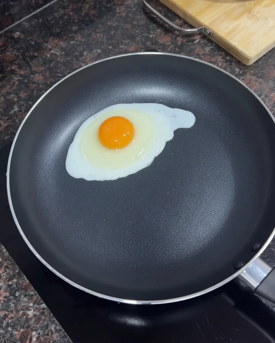 Ein einzelnes Ei brät in einer schwarzen Pfanne mit geschmolzener Butter.