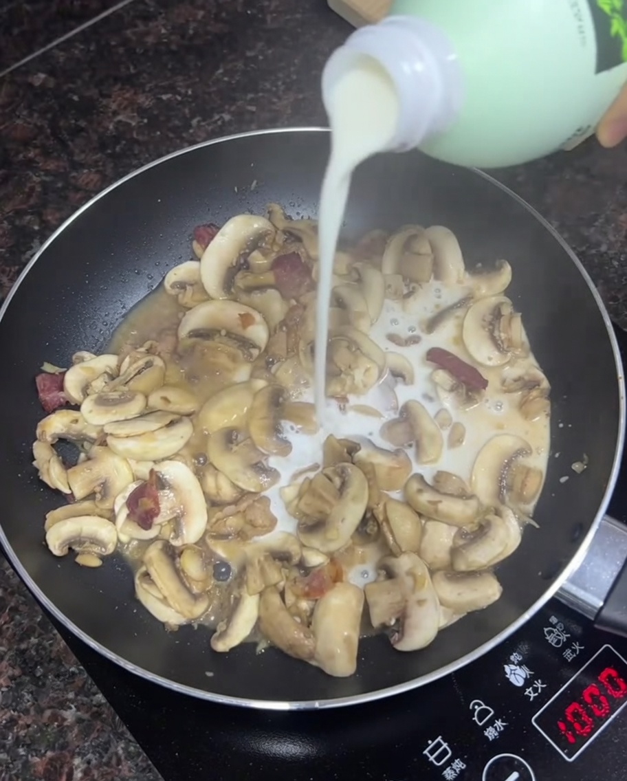 Milch wird in die Pfanne mit sautierten Pilzen und Speck gegossen.
