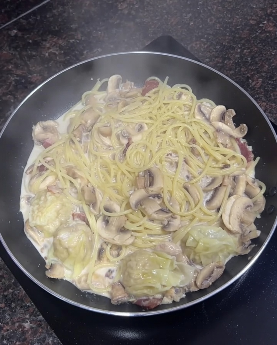 Pfanne mit cremigen Spaghetti, Pilzen und einigen gekochten Wontons.