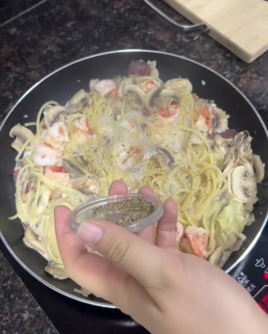 Eine Hand streut frischen schwarzen Pfeffer über eine Pfanne mit cremiger Pasta.