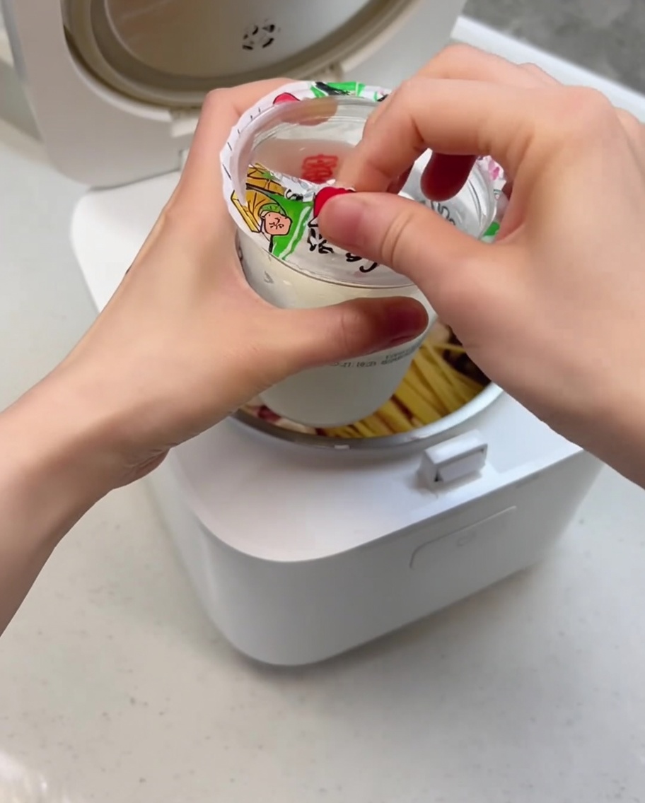 Nahaufnahme, wie das cremige Eis in den Reiskochertopf über die anderen Zutaten gegossen wird.