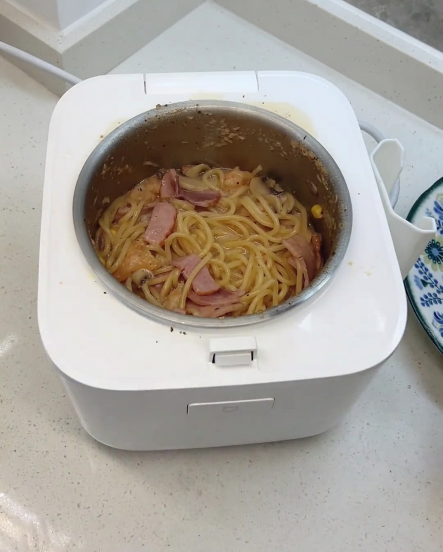Die fertigen cremigen Pilz-Spaghetti werden mit Käse und Milchwürfeln im Reiskocher umgerührt.