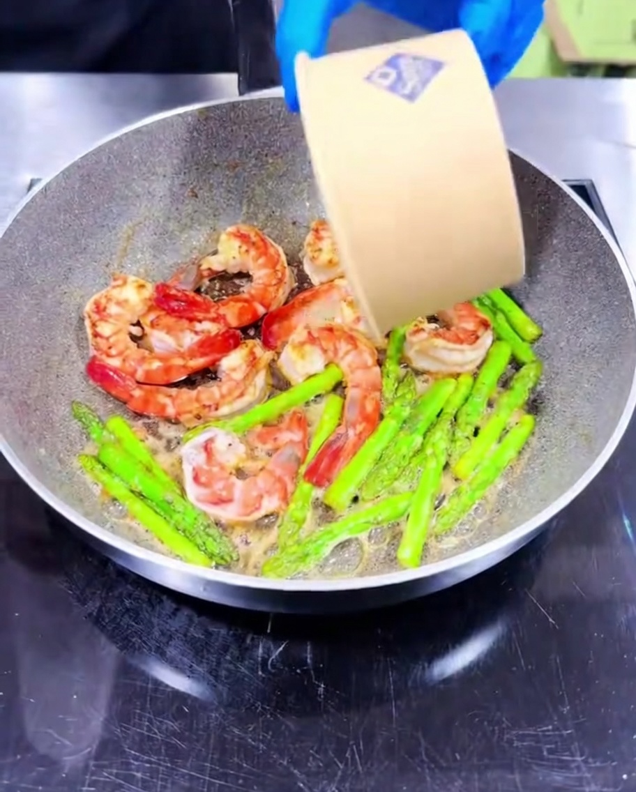 Gehackter Knoblauch wird unter die garenden Garnelen und den Spargel gerührt.