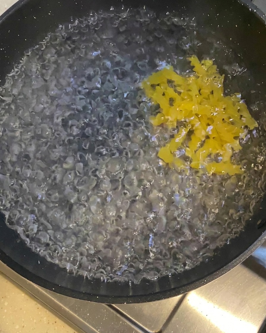 Gelbe, gedrehte Nudeln in einem dunklen Topf mit sprudelnd kochendem Wasser.