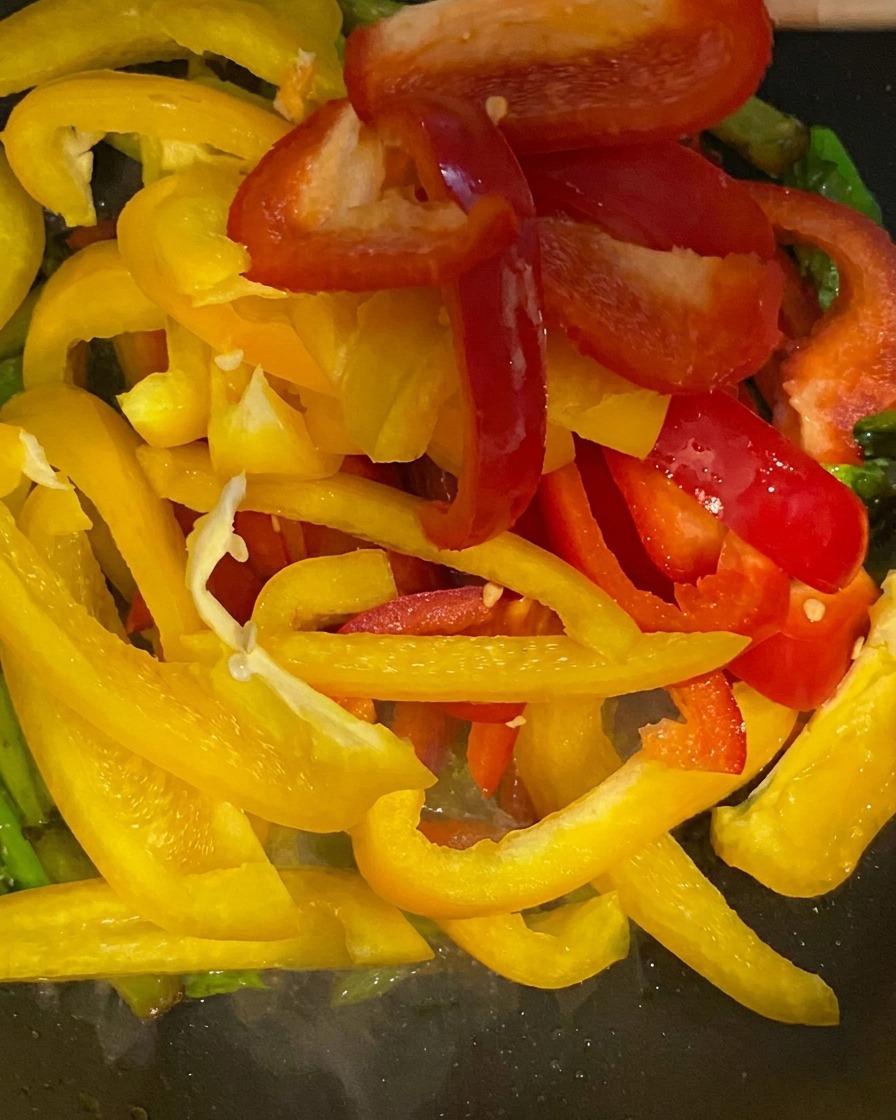 Rote und gelbe Paprikastreifen werden zum grünen Spargel in die Pfanne gegeben.