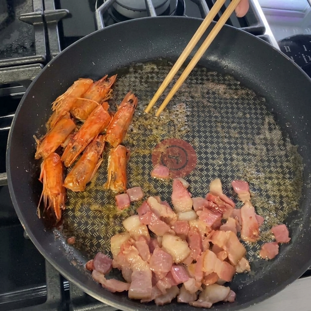 Große, geschälte Garnelen werden zusammen mit Speck und Köpfen in die Pfanne gegeben.