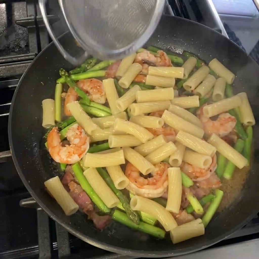 Gekochte Rigatoni werden in die Pfanne zu Spargel und Garnelen gegeben.