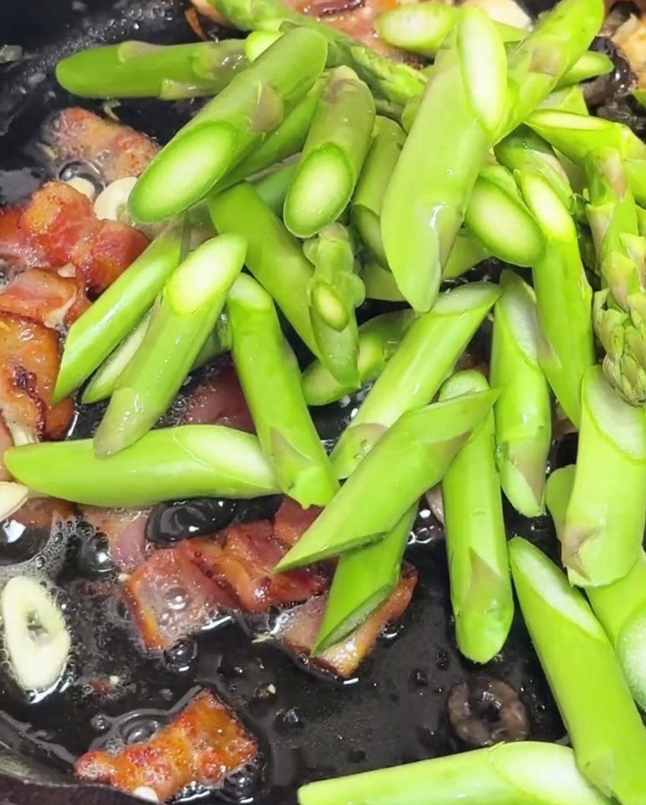 Spargelstücke und halbierte Kirschtomaten werden zusammen mit Speck und Knoblauch in der Pfanne angebraten.