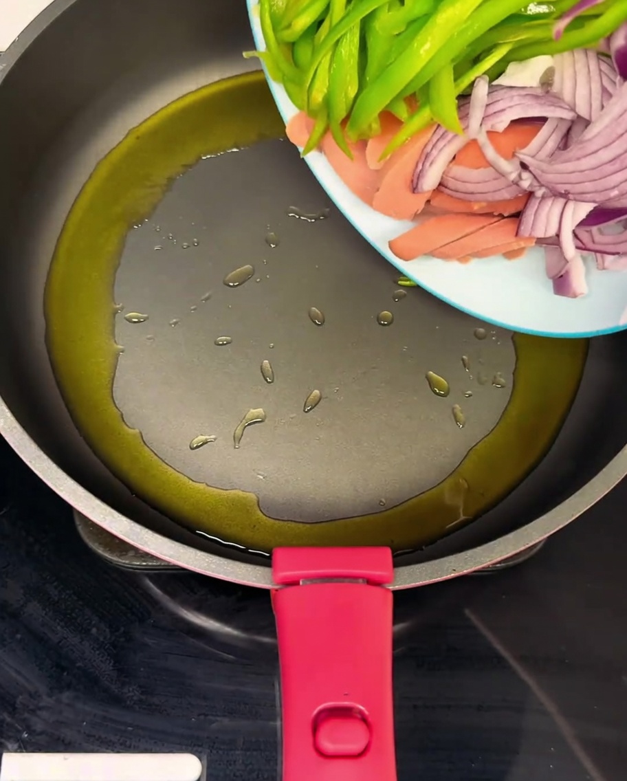Eine heiße Pfanne mit Schinkenstreifen, grüner Paprika und Zwiebeln, die in Öl geschwenkt werden.