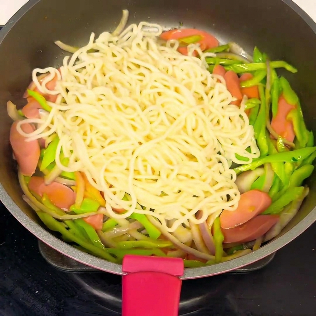 Eine Pfanne voller Nudeln und Gemüse, in der die Sauce über die Mischung gegossen wird.