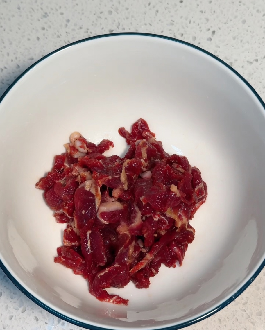 Dünn geschnittenes Rindfleisch wird in einer weißen Schüssel gründlich mit den Marinadenzutaten vermengt.