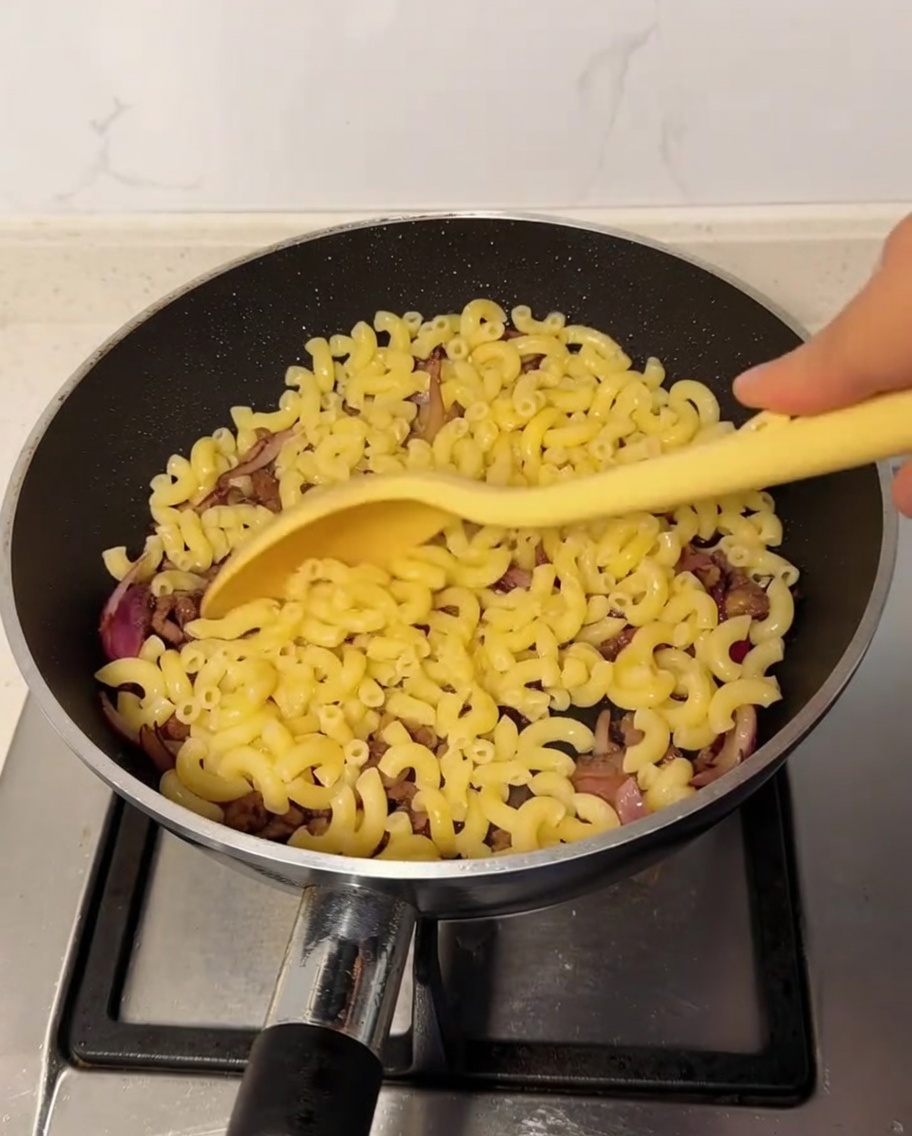 Gekochte Makkaroni werden in der Pfanne unter die Rindfleisch-Zwiebel-Mischung gehoben.