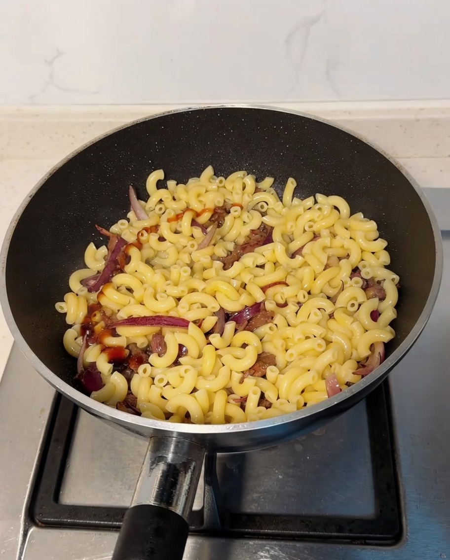 Austernsauce und helle Sojasauce werden über die Makkaroni-Rindfleisch-Mischung in der Pfanne geträufelt.