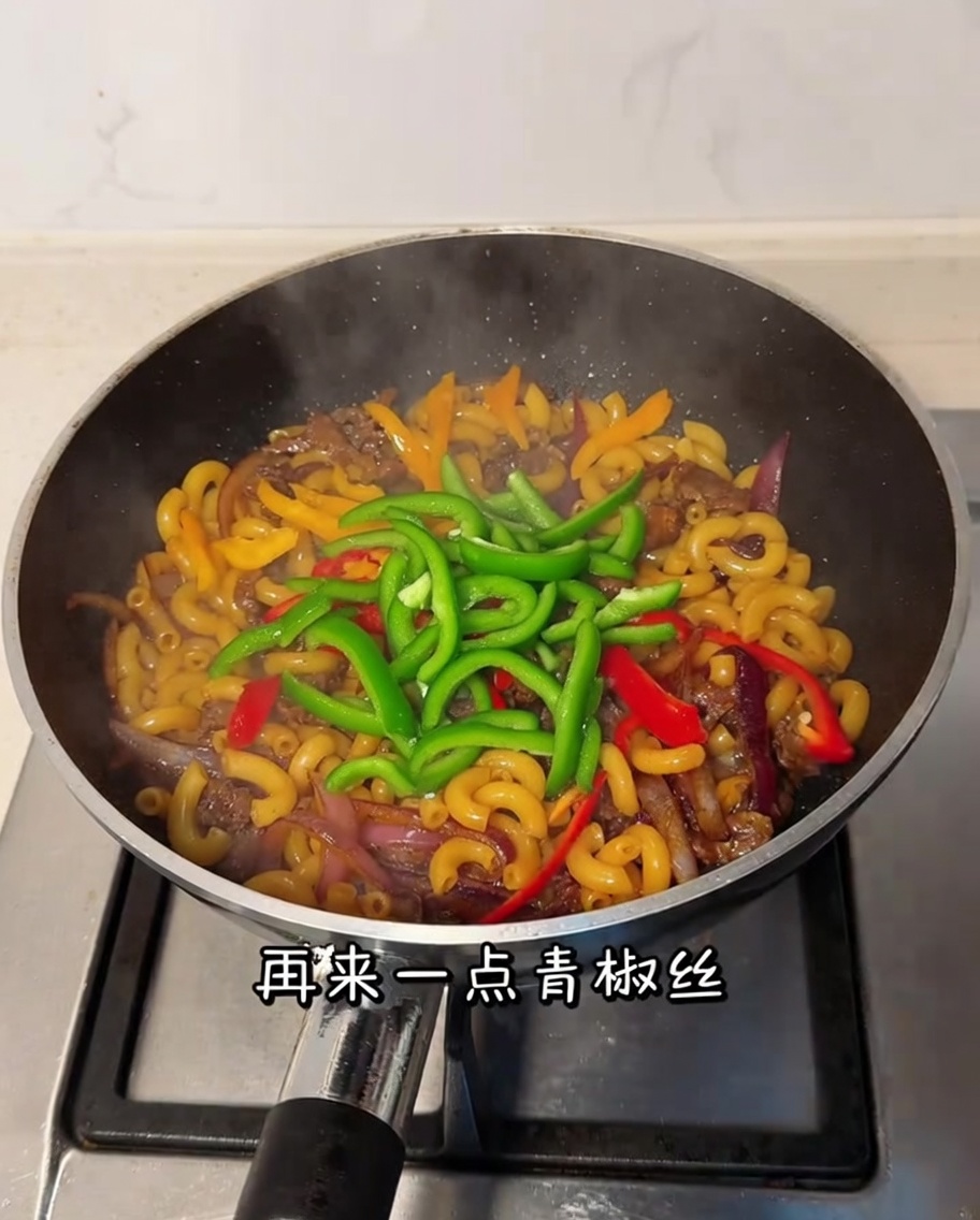 Geschnittene grüne Paprika wird in der Pfanne unter die Makkaroni und das Rindfleisch gerührt.