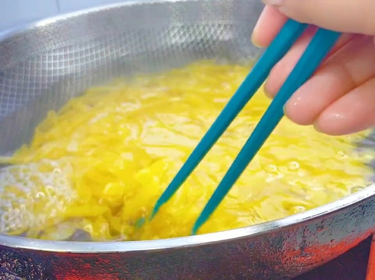 Blaue Stäbchen rühren kochende Penne-Pasta in einem großen Edelstahl-Wok um.