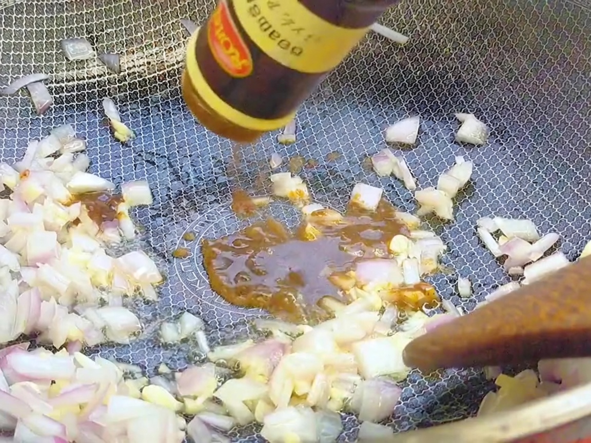 Schwarze Pfeffersauce wird aus einer Flasche in den Wok zu den angebratenen Aromaten gegeben.