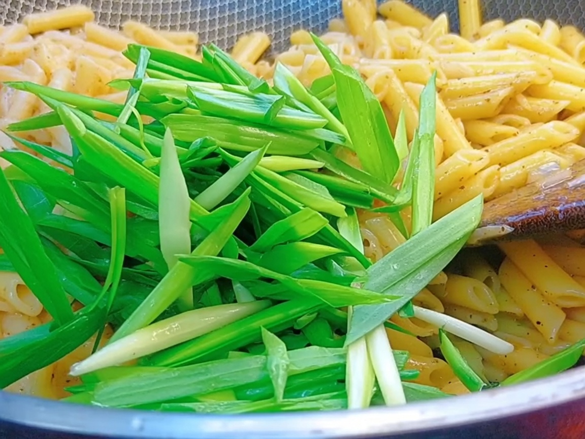 Frische grüne Knoblauchsprossen werden in den Wok mit Pasta und Pfeffersauce gegeben.