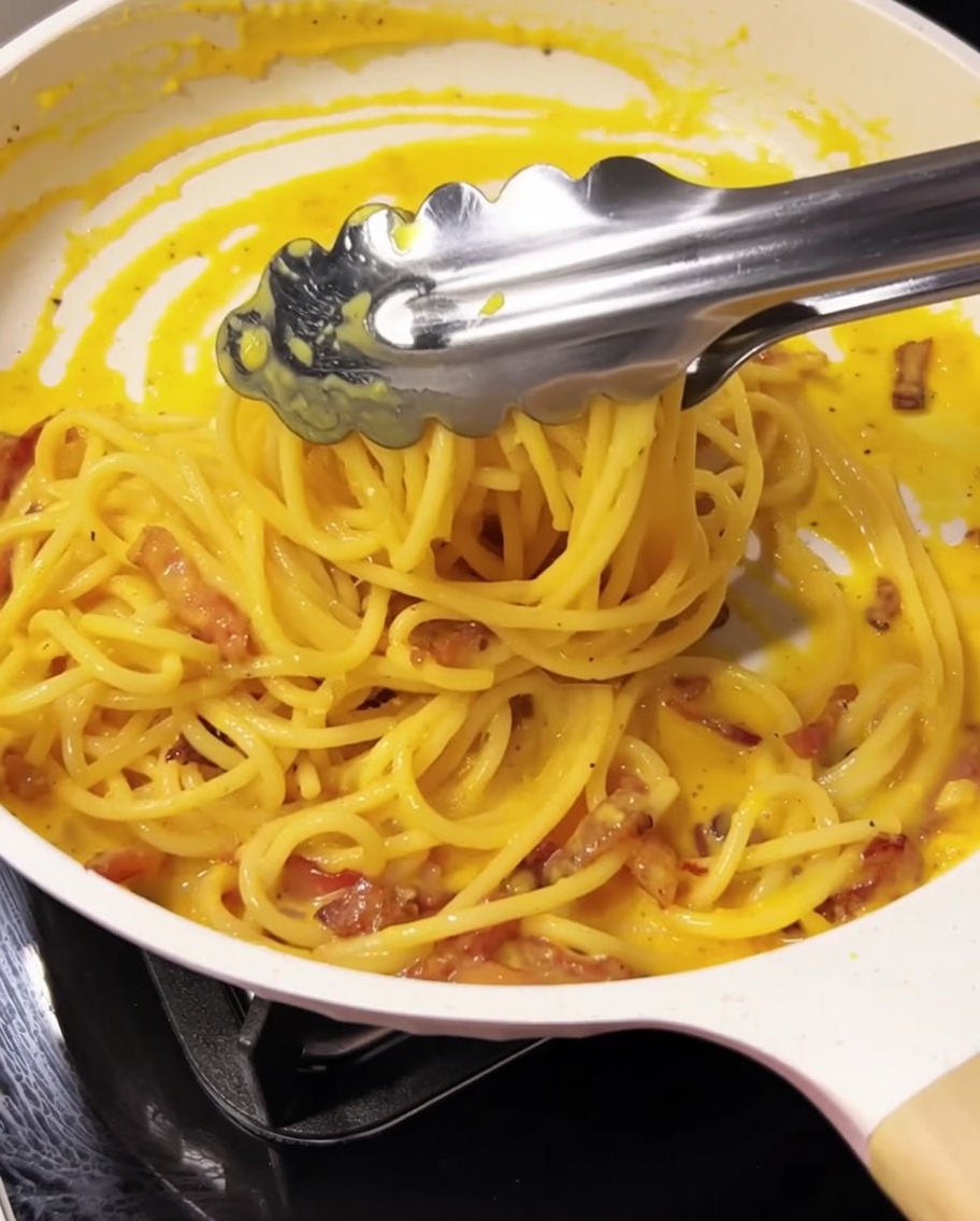Spaghetti werden mit einer Zange in der Pfanne geschwenkt.