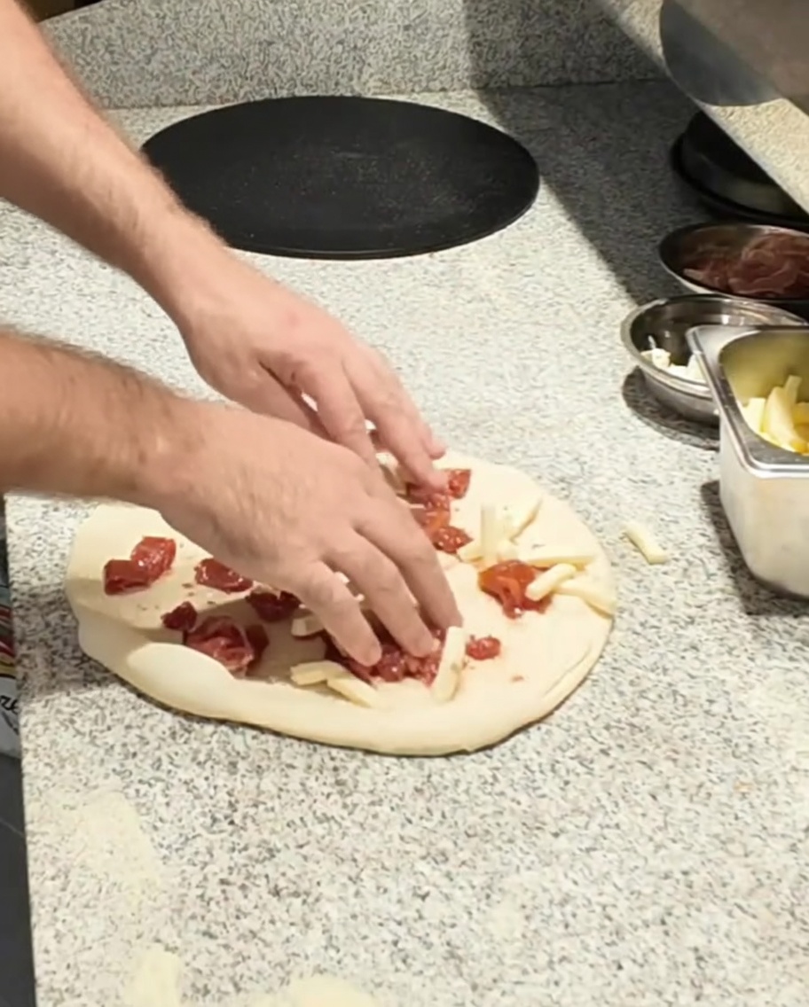 Mozzarellastücke werden auf dem Pizzateig verteilt.