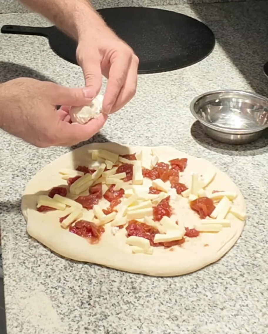 Frischer Ziegenkäse wird auf die Pizza gegeben.