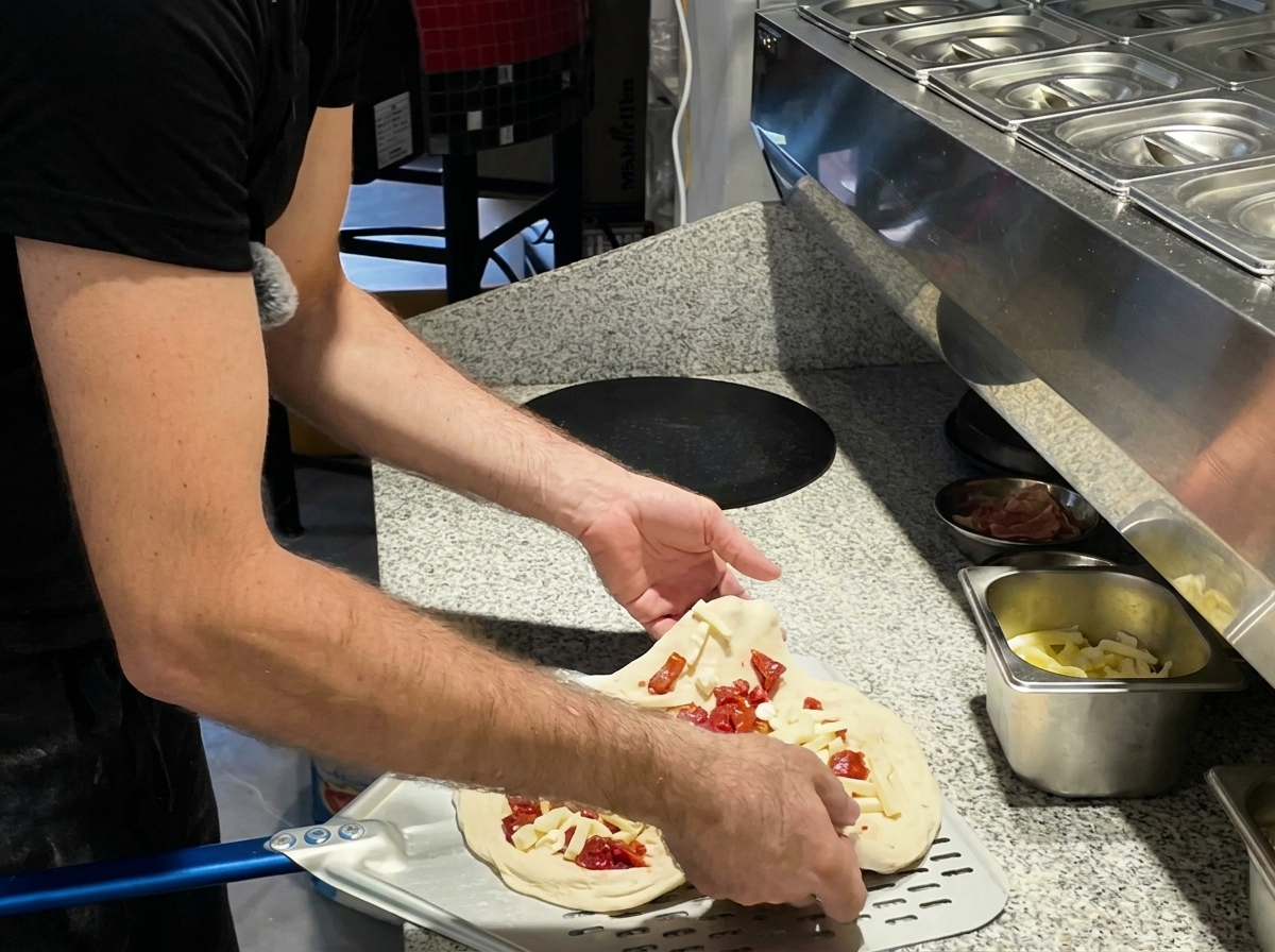 Eine Pizza wird mit einem Metallschieber in den Ofen geschoben.