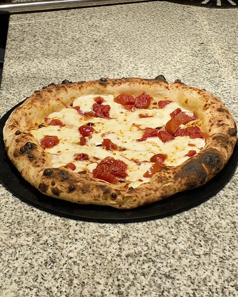 Die fertige Pizza auf einer dunklen Oberfläche wird mit Pancettascheiben belegt.